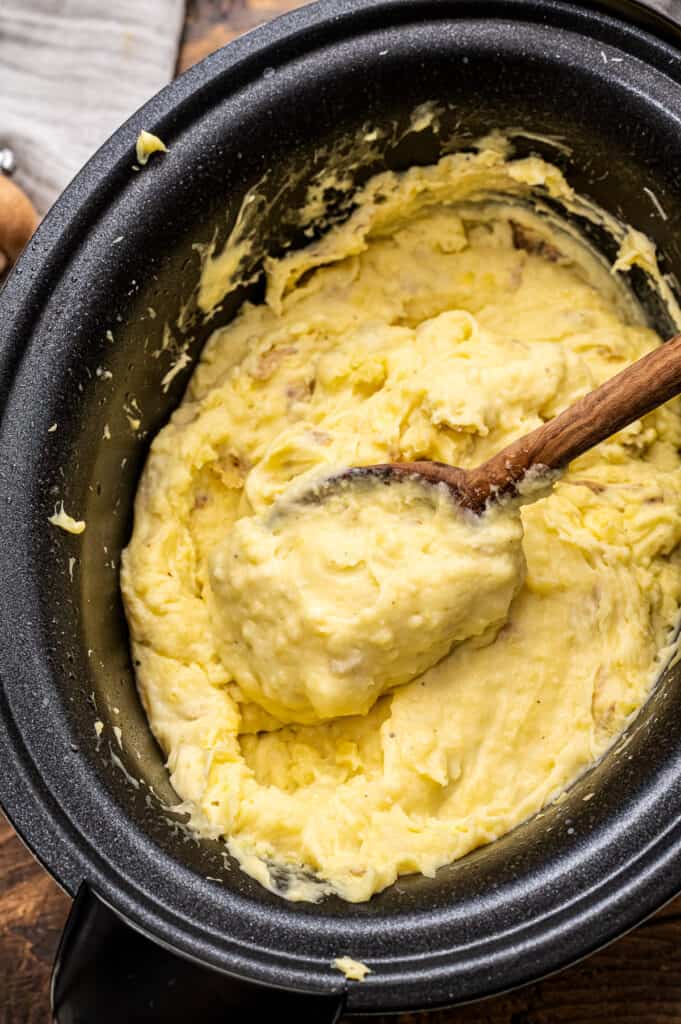 Wooden spoon in Crockpot full of mashed potatoes
