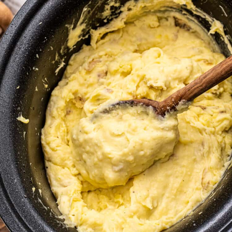 Wooden spoon in Crockpot full of mashed potatoes