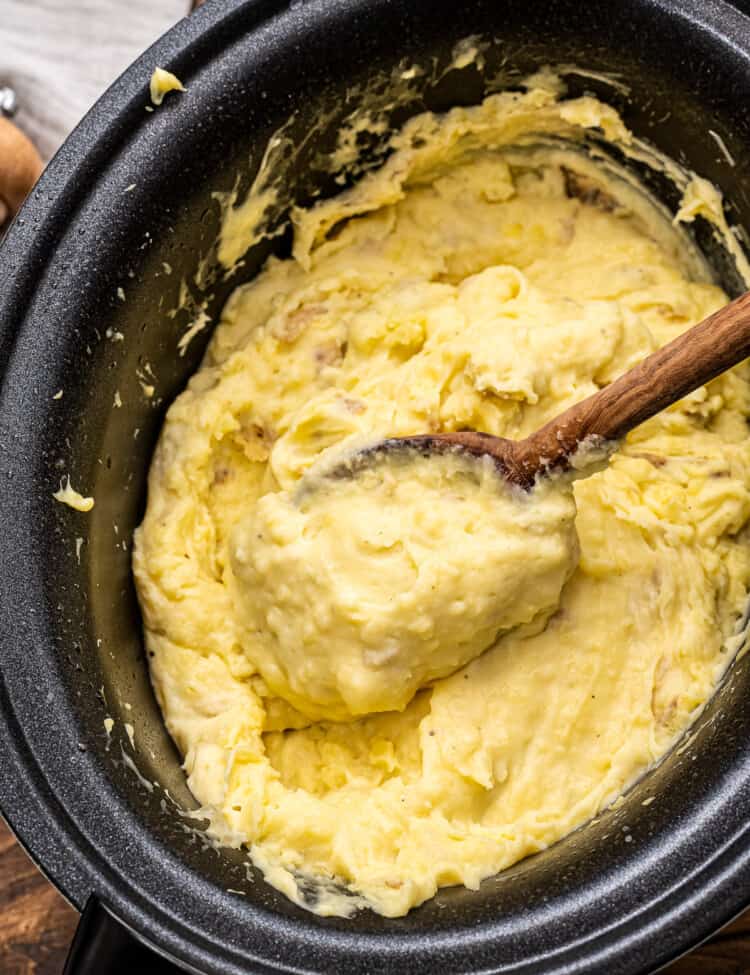 Wooden spoon in Crockpot full of mashed potatoes