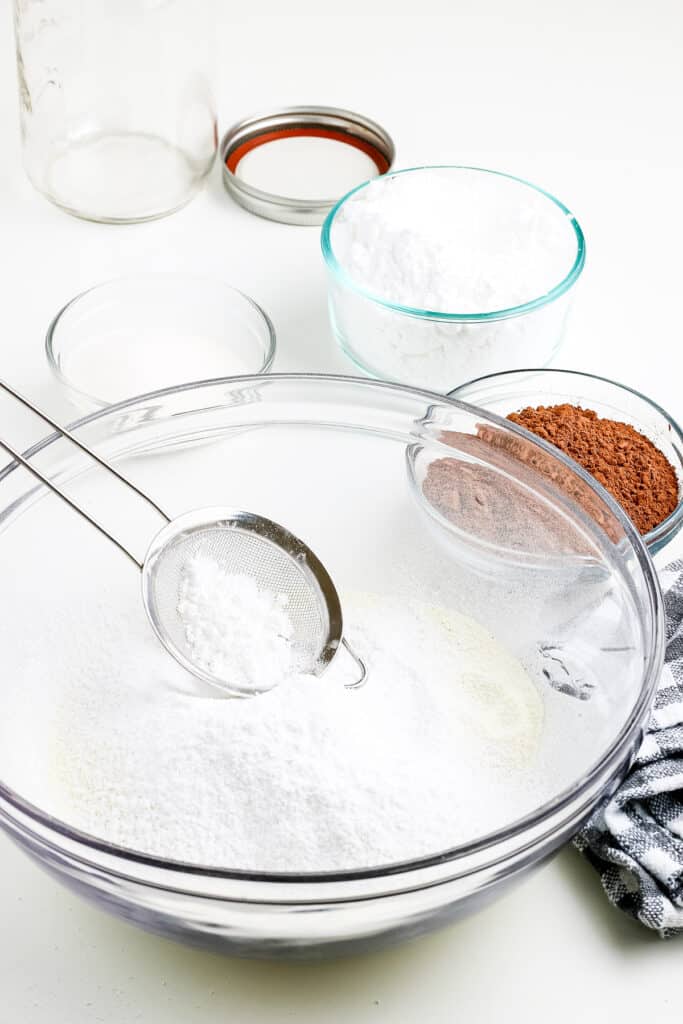 Glass bowl with powdered sugar with sifter sitting on top of it