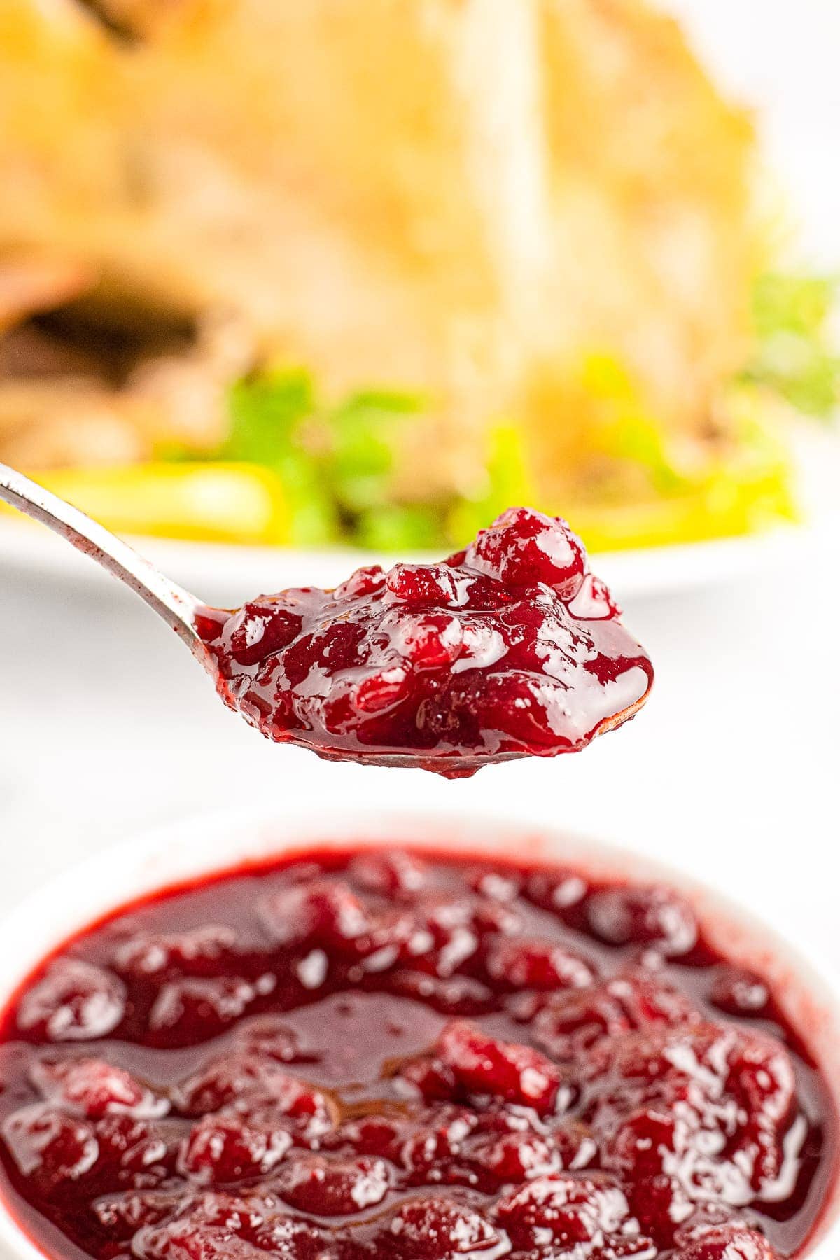 Instant Pot Cranberry Sauce on a spoon with bowl of it in background