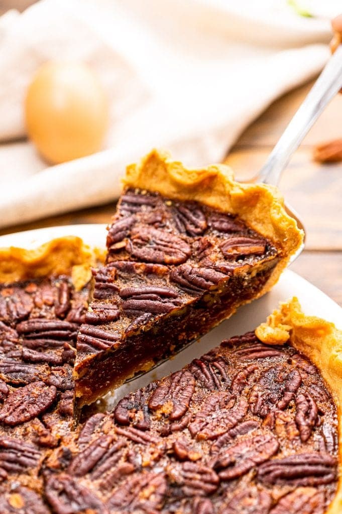 Piece of pecan pie being lifted out of pie in a white pie dish.