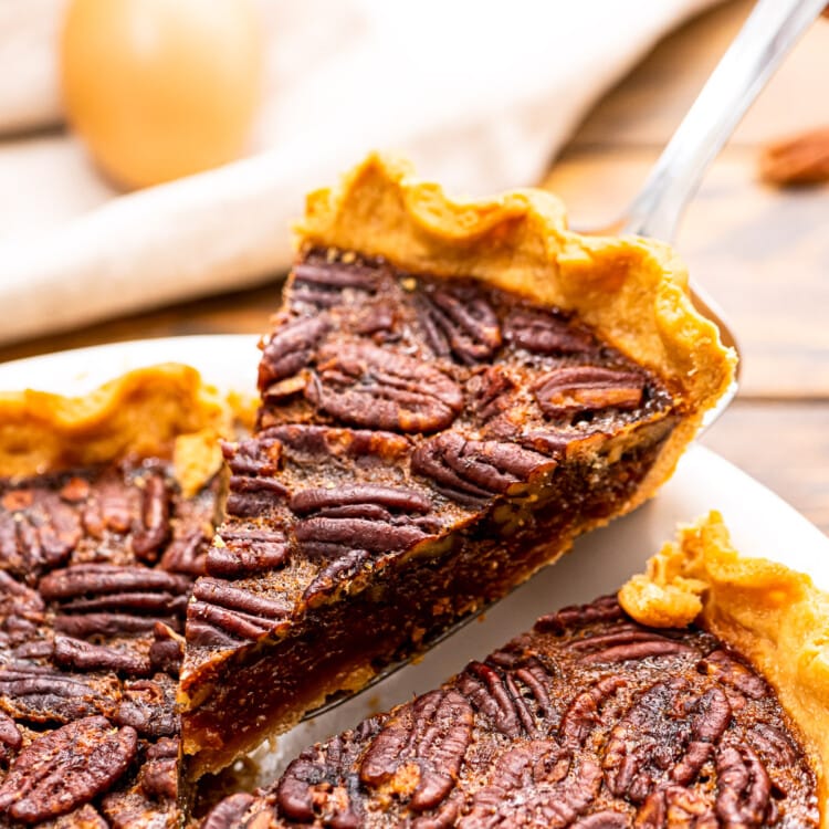 Piece of pecan pie being lifted out of pie in a white pie dish.