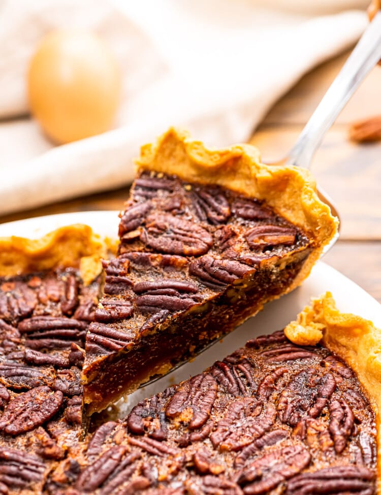 Piece of pecan pie being lifted out of pie in a white pie dish.