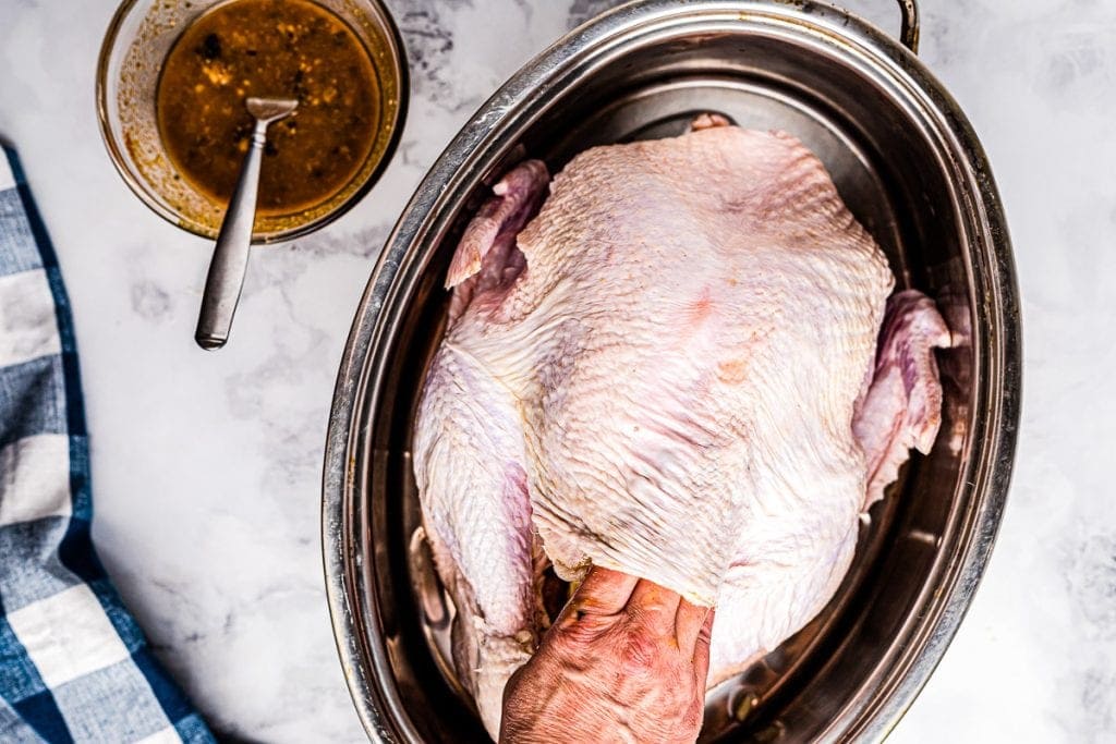 Roast Turkey in Pan with seasonings being rubbed under skin