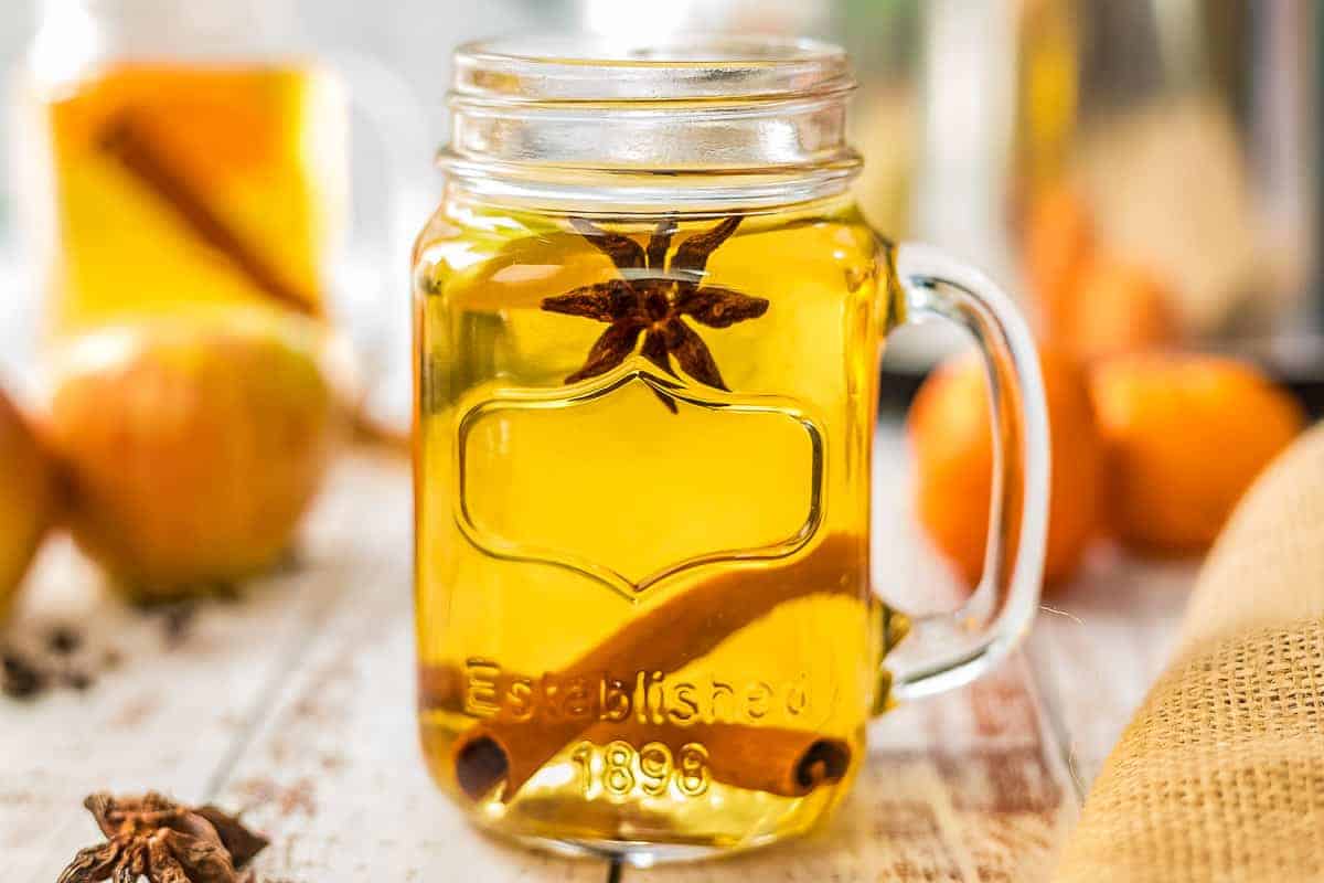 Glass Mason Jar filled with spiked apple cider with whole cinnamon stick and star anise in the mug