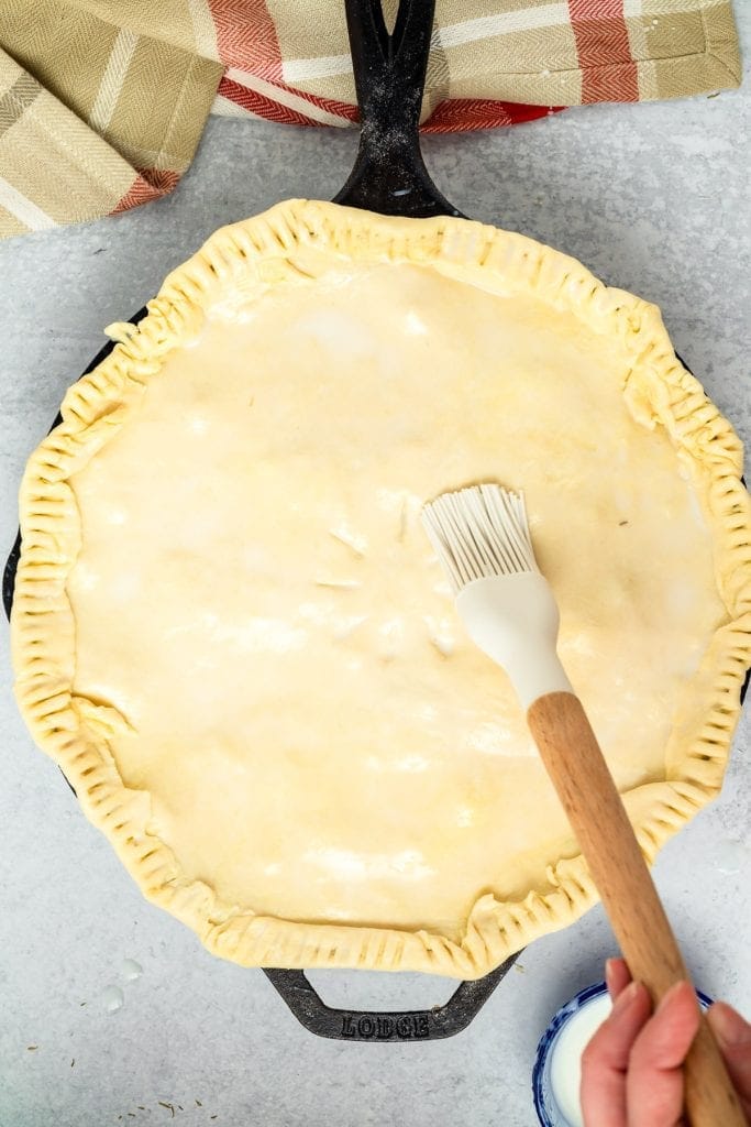 Pastry brush brushing butter over puff pastry crust on pot pie