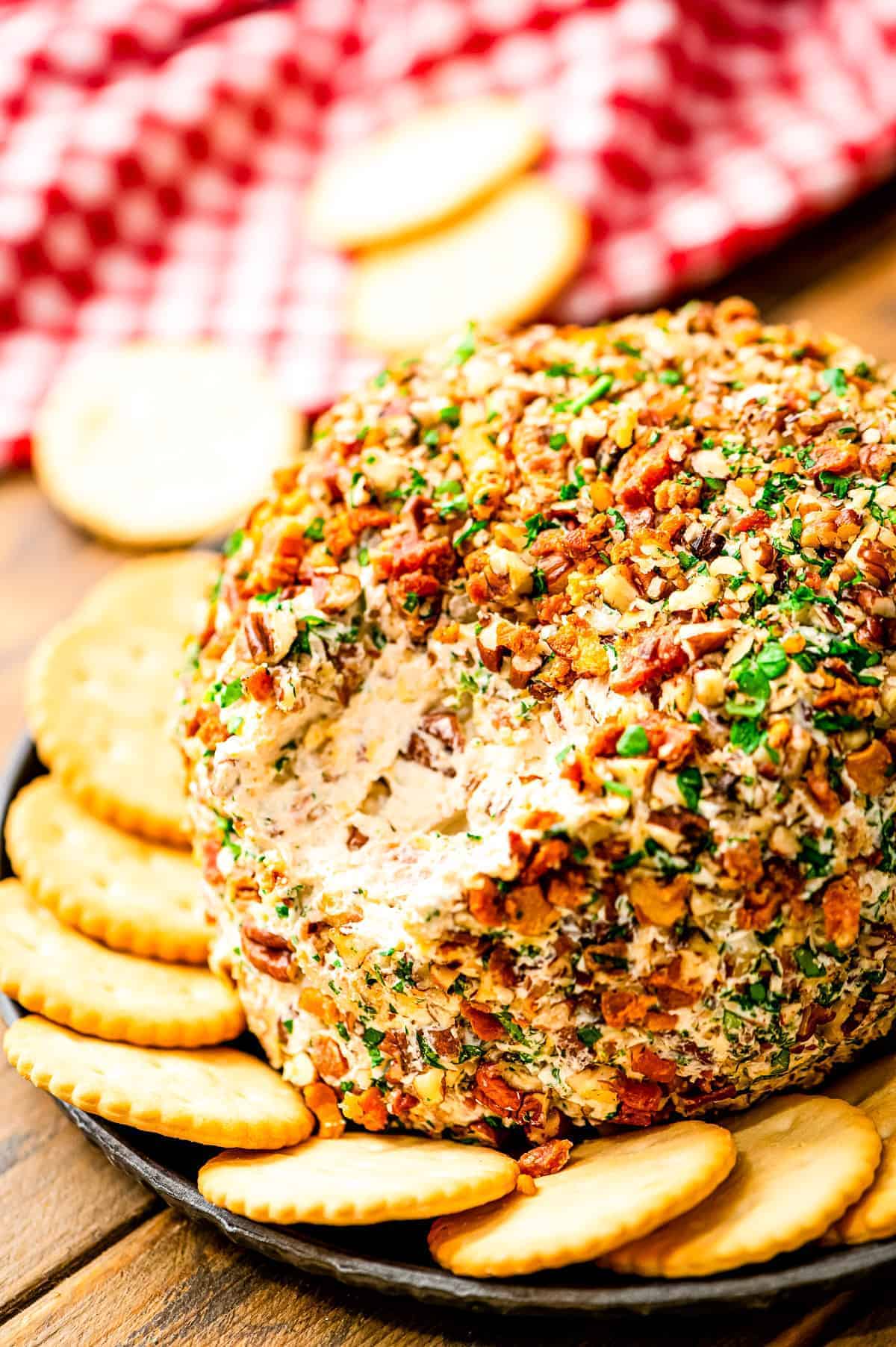 Bacon Ranch Cheese Ball with a scoop taken out of it on plate with crackers