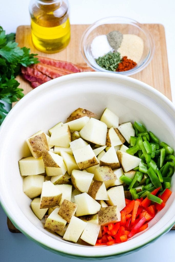 White bowl with diced potatoes, red and green peppers before stirring.