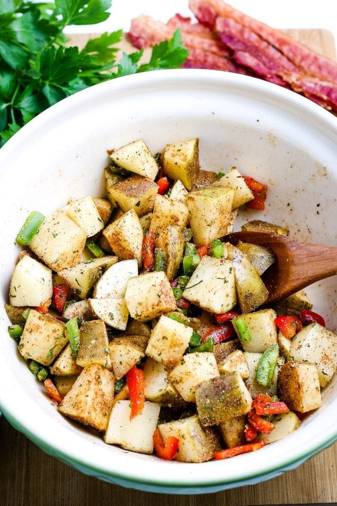 White bowl with a wooden spoon stirring breakfast potato ingredients together.