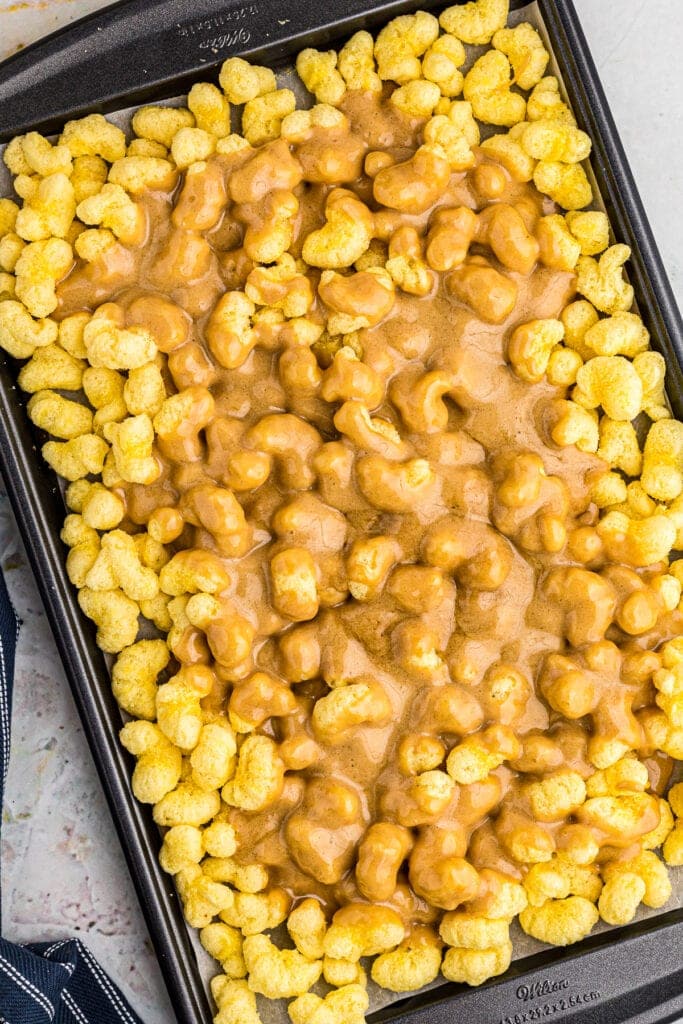 Puff Corn on baking sheet covered with caramel sauce before stirring.