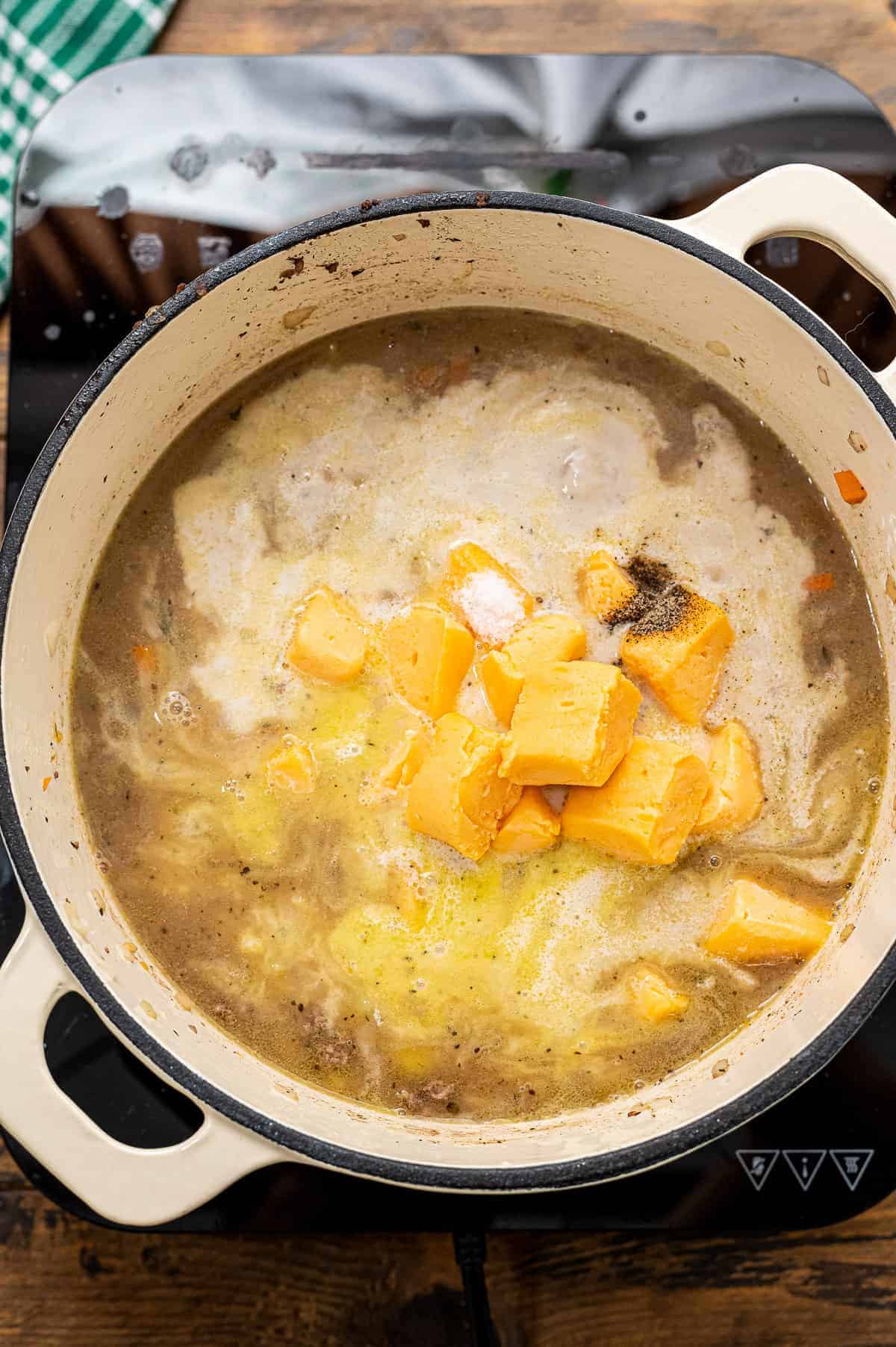 Stock pot with soup and cubes of cheese before melting.