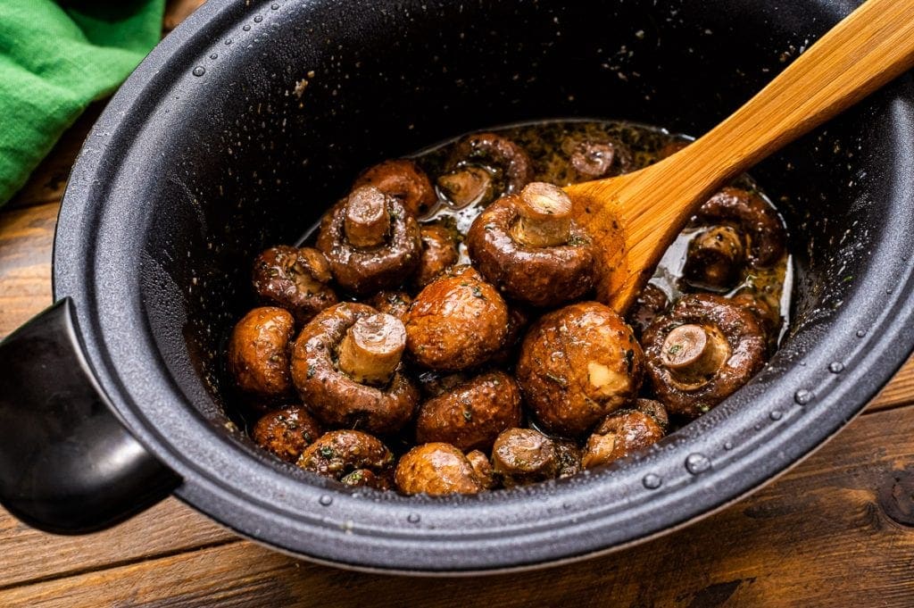 Crock Pot with cooked ranch mushrooms in it and a wooden spoon.