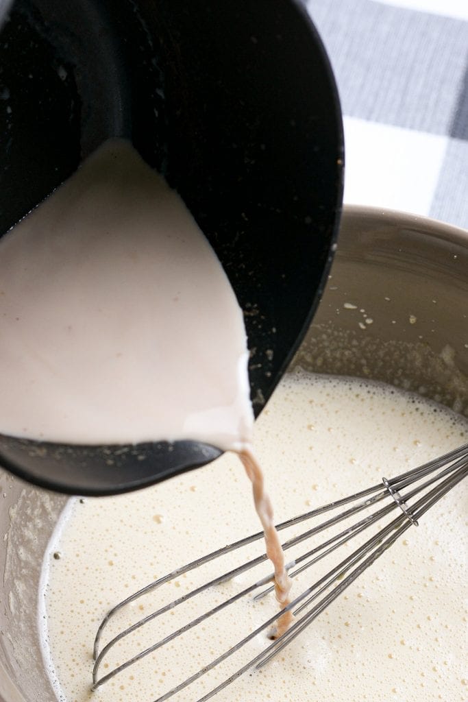 Pouring heated milk into egg mixture for eggnog