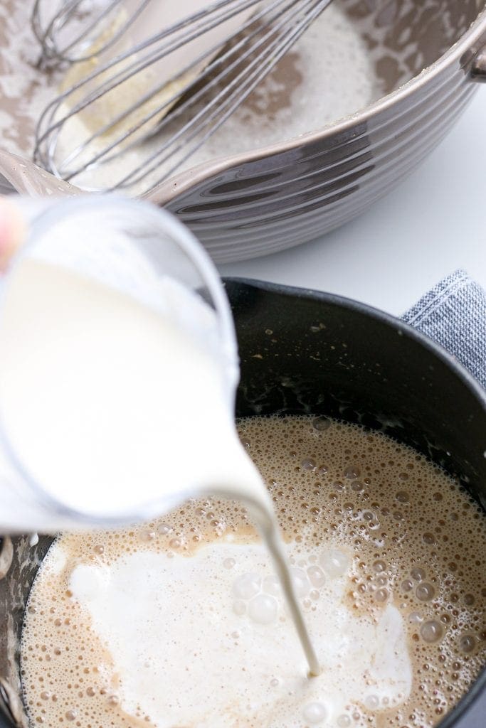 Adding cream into heated eggnog in saucepan.