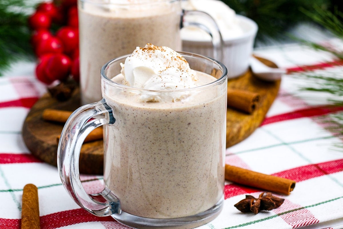 Mug with homemade eggnog topped with whipped cream and more in background