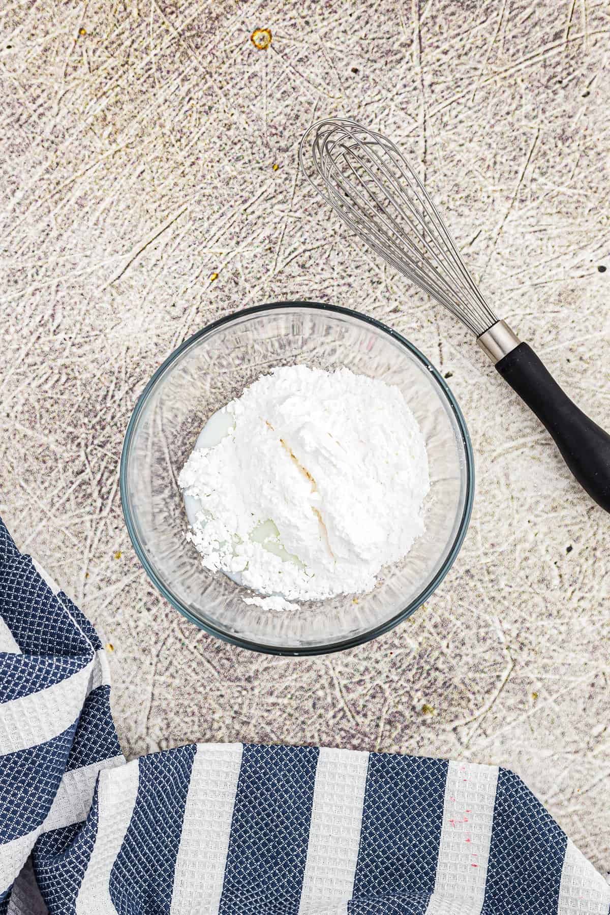 Glass bowl with powdered sugar and milk in it before mixing.