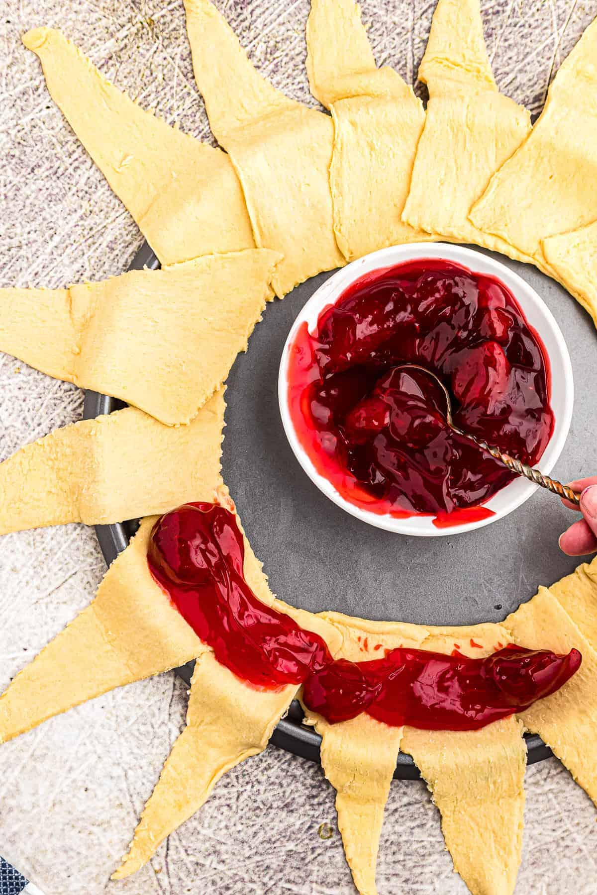 Crescent rolls in a ring shape being topped with strawberry pie filling