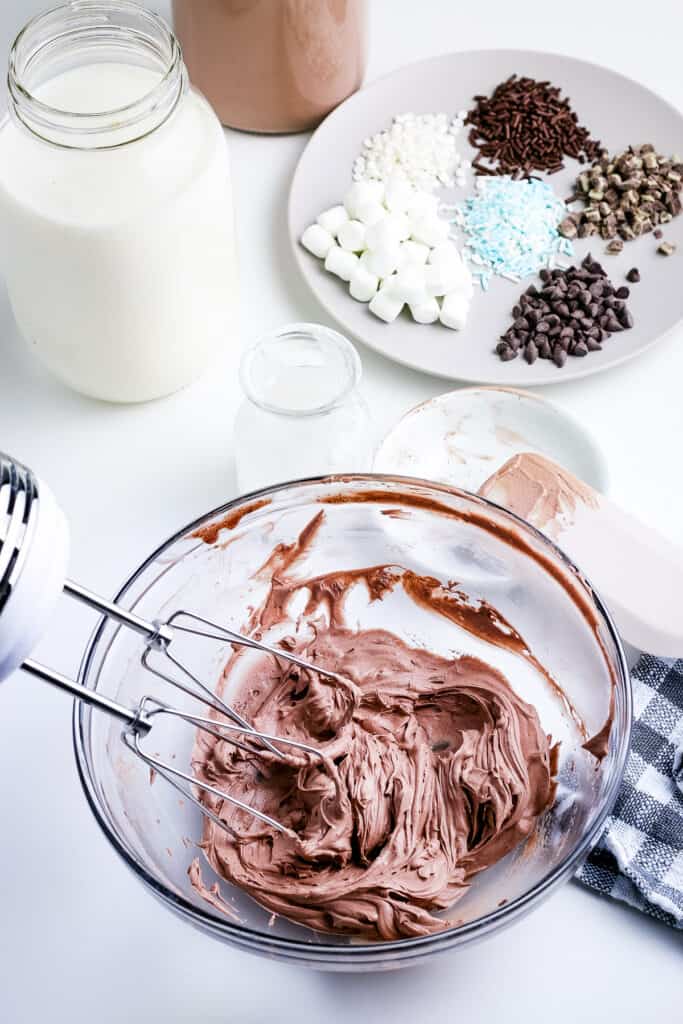 Hand mixer making whipped hot chocolate in glass bowl