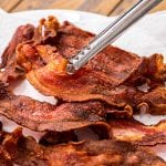 Metal tongs holding a piece of crispy bacon