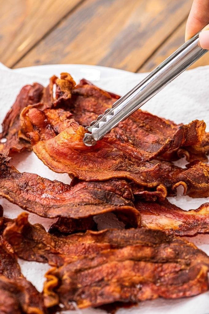 Metal tongs holding a piece of crispy bacon