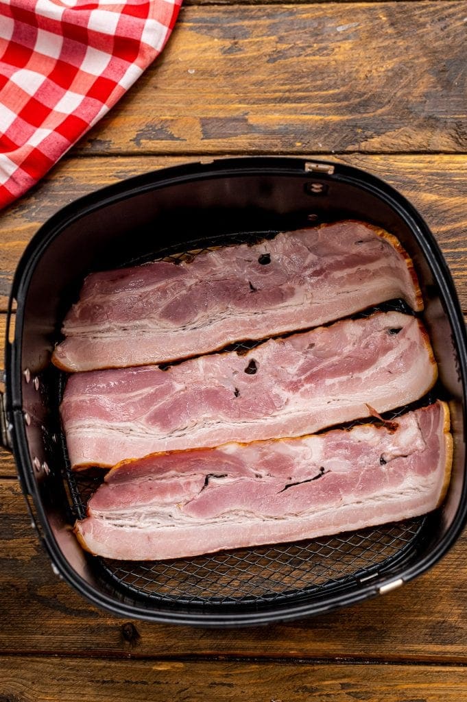 Air Fryer Basket with uncooked bacon strips in it.