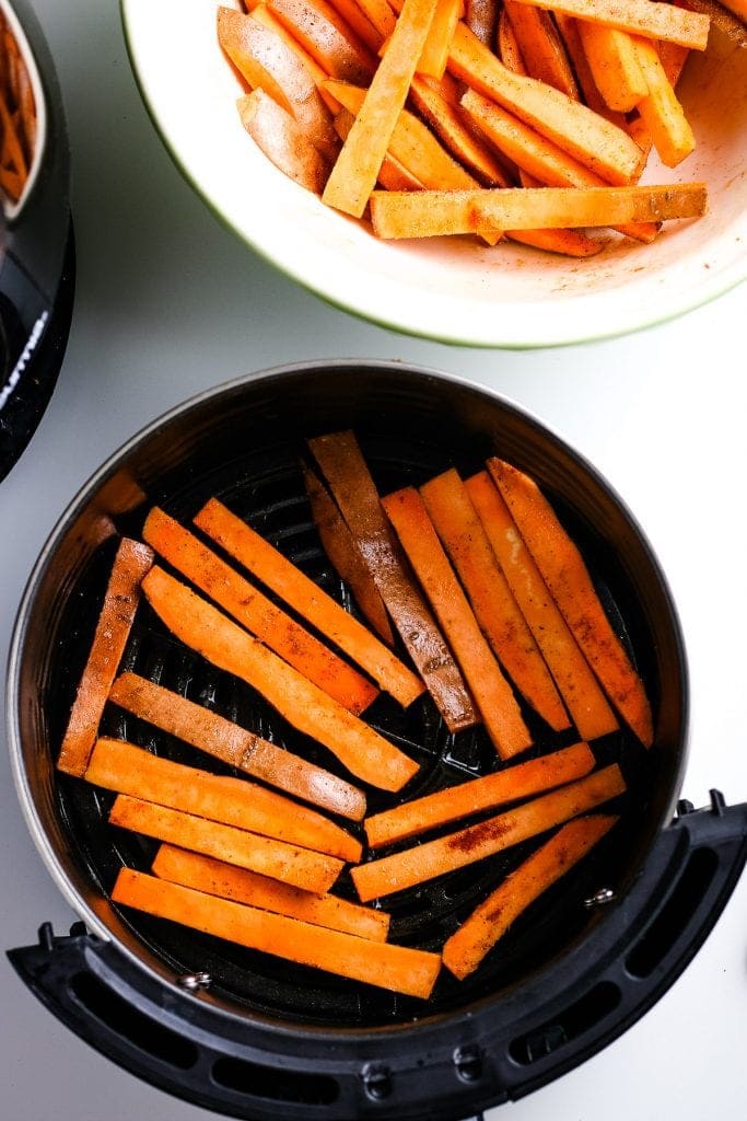 An air fryer basket with raw sweet potatoes fries in it.