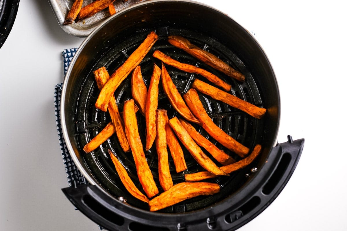 An air fryer basket with cooked sweet potatoes fries in it.