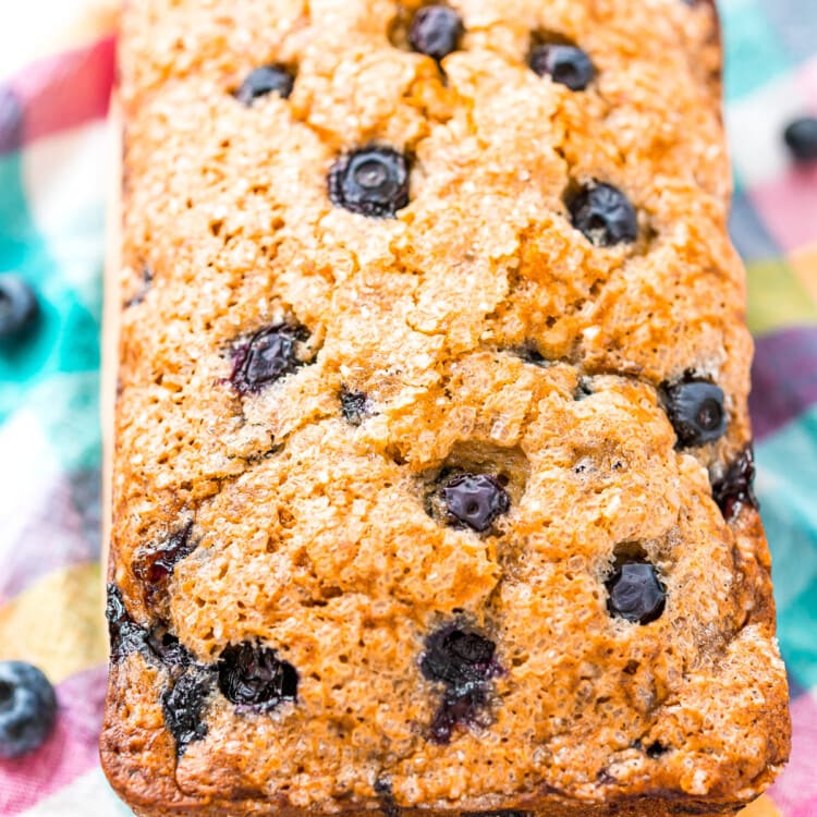 A loaf of baked Blueberry Banana Bread on wooden cutting board.