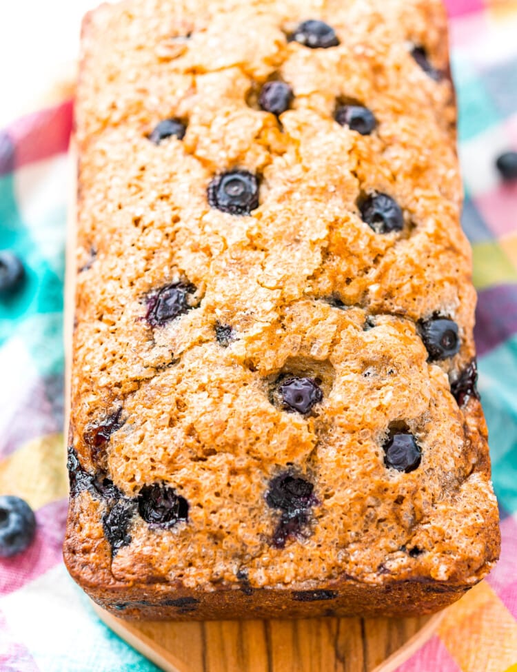 A loaf of baked Blueberry Banana Bread on wooden cutting board.