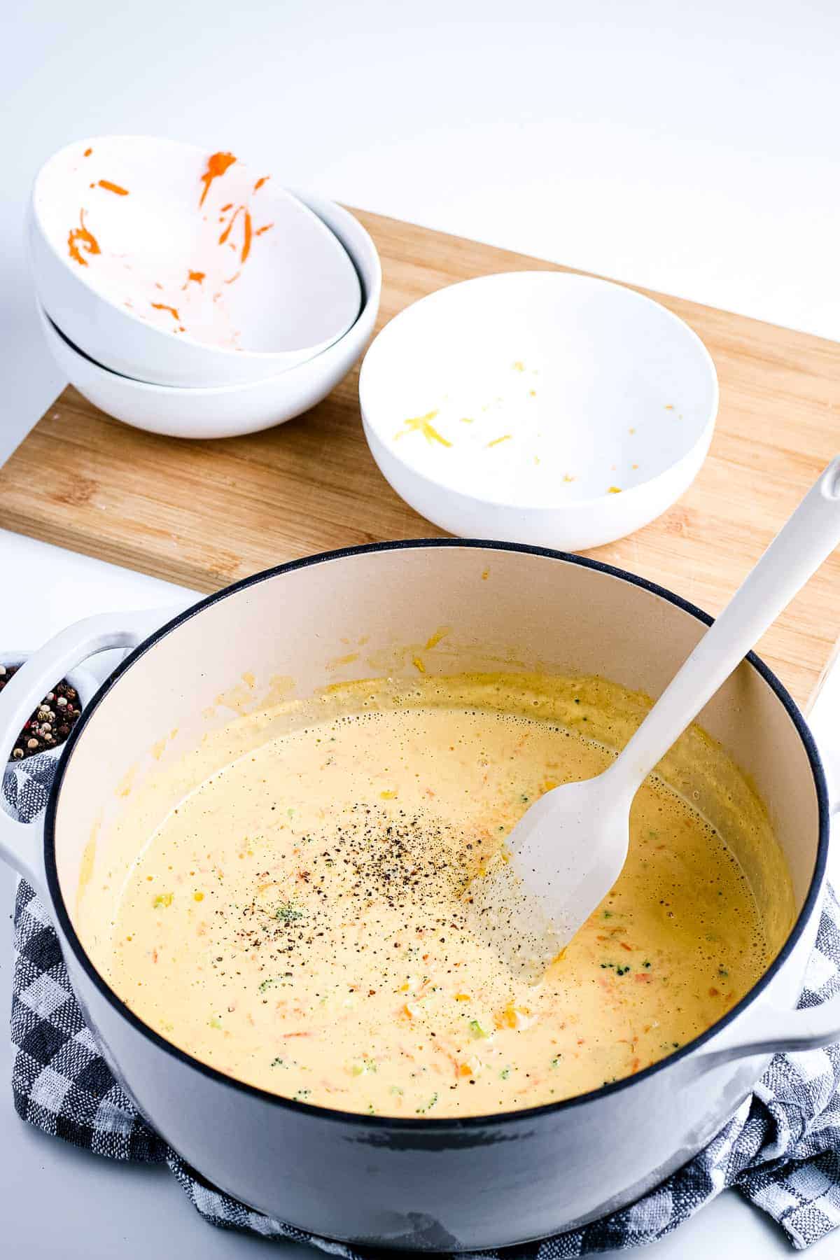 Dutch oven with a spoon and cheesy broccoli soup in it seasoned with pepper.