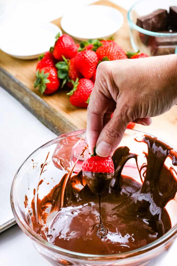 Hand dipping strawberry in melted chocolate