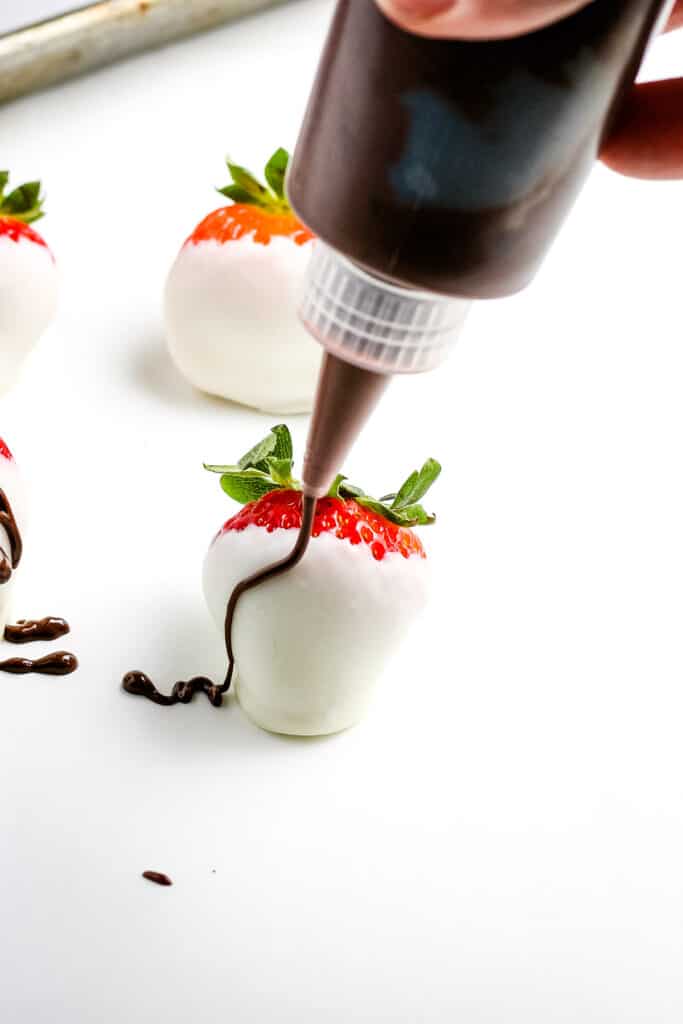 Piping melted chocolate onto strawberry with white chocolate