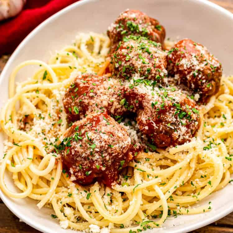 Square Image showing crock pot meatballs served over spaghetti noodles