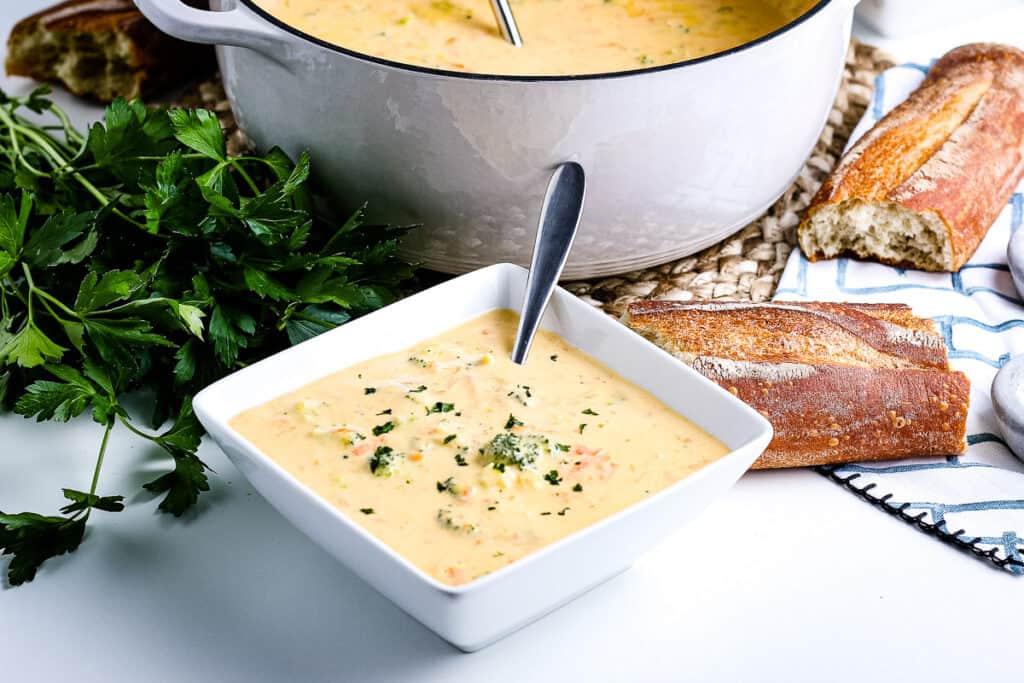 Square white bowl with broccoli cheese soup in it and spoon