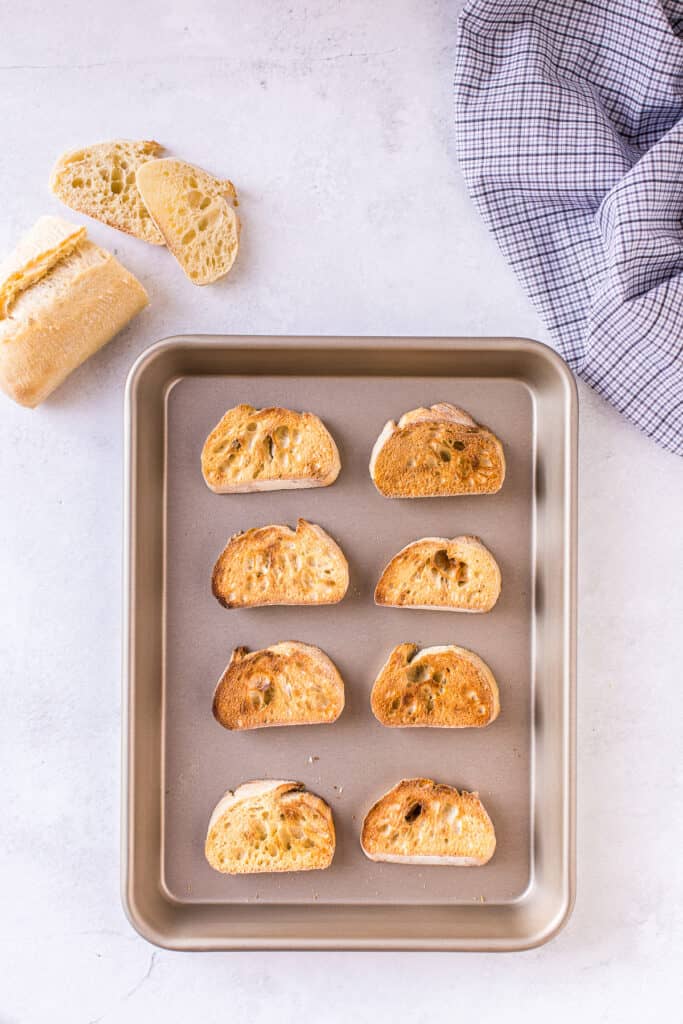 Sliced and toasted baguette on baking sheet