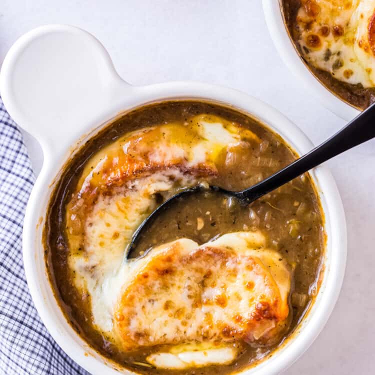 Spoon taking a bite of French Onion Soup with toasted baguette and melted cheese