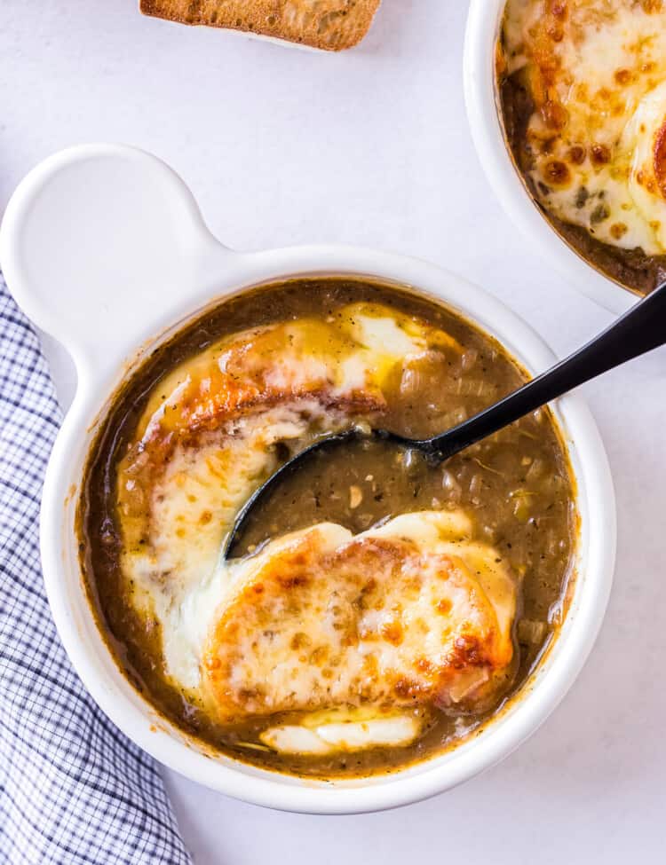 Spoon taking a bite of French Onion Soup with toasted baguette and melted cheese