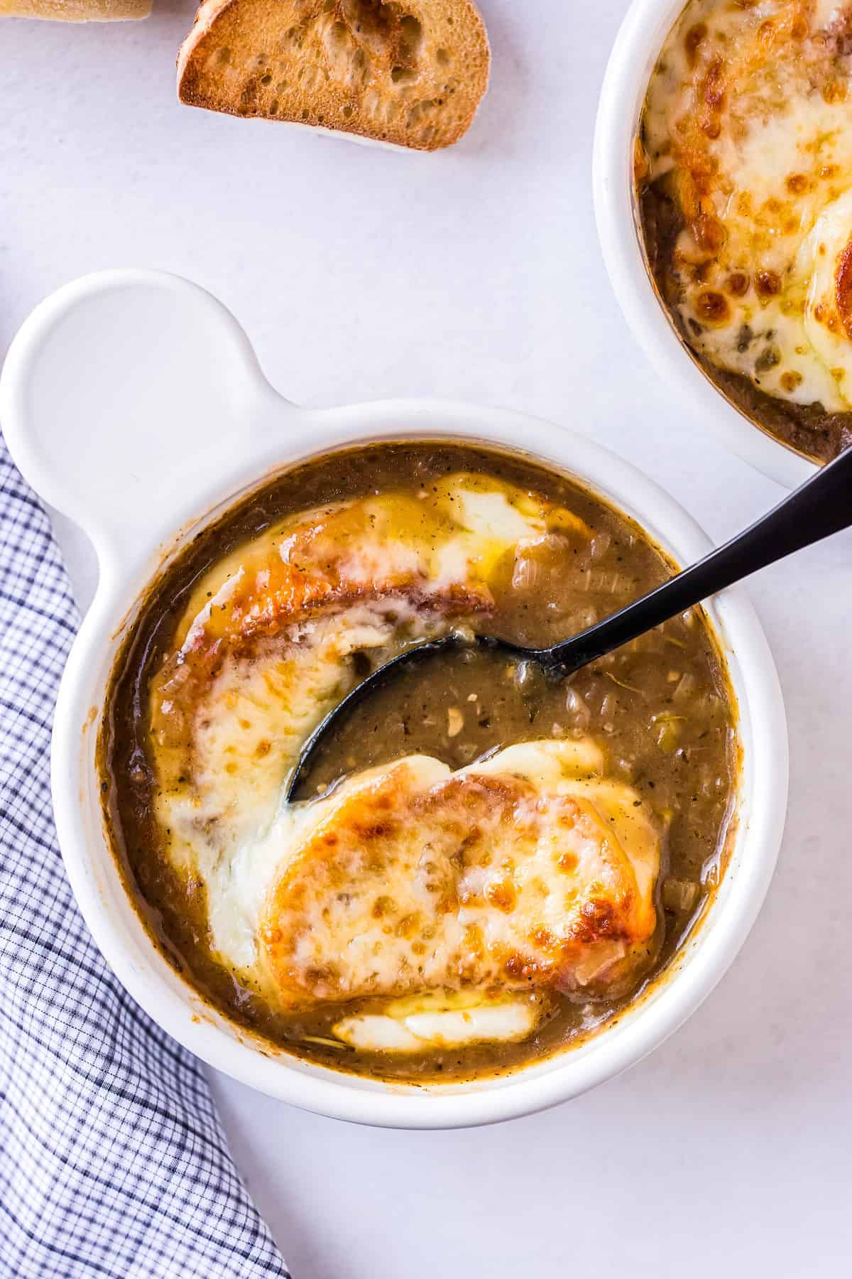 Spoon taking a bite of French Onion Soup with toasted baguette and melted cheese