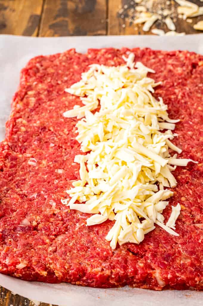 Italian Meatloaf ingredients spread out into rectangle with shredded Mozzarella cheese in middle