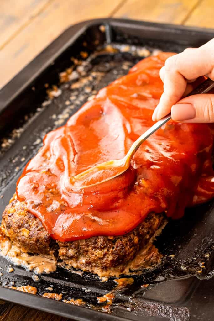 Spoon spreading tomato sauce on top of Italian meatloaf