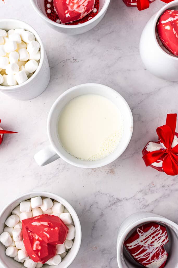 White mugs with milk, marshmallows and hot cocoa bombs
