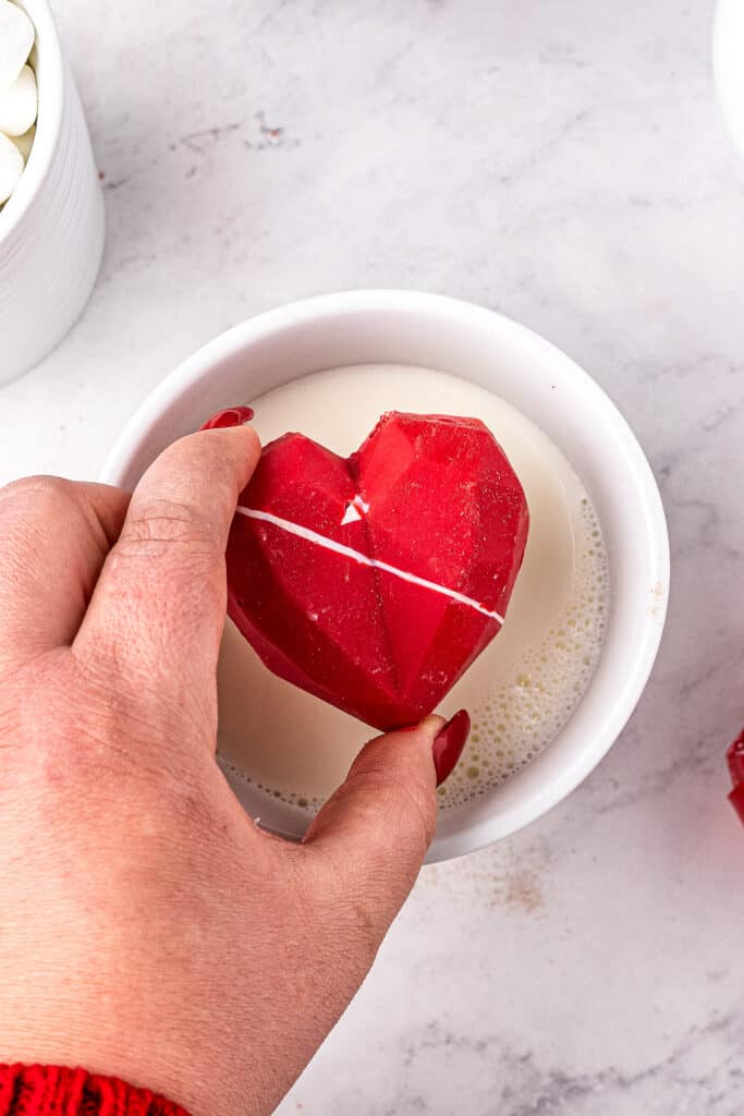 Hand dropping Valentine's Day Hot Chocolate Bomb into mug of milk