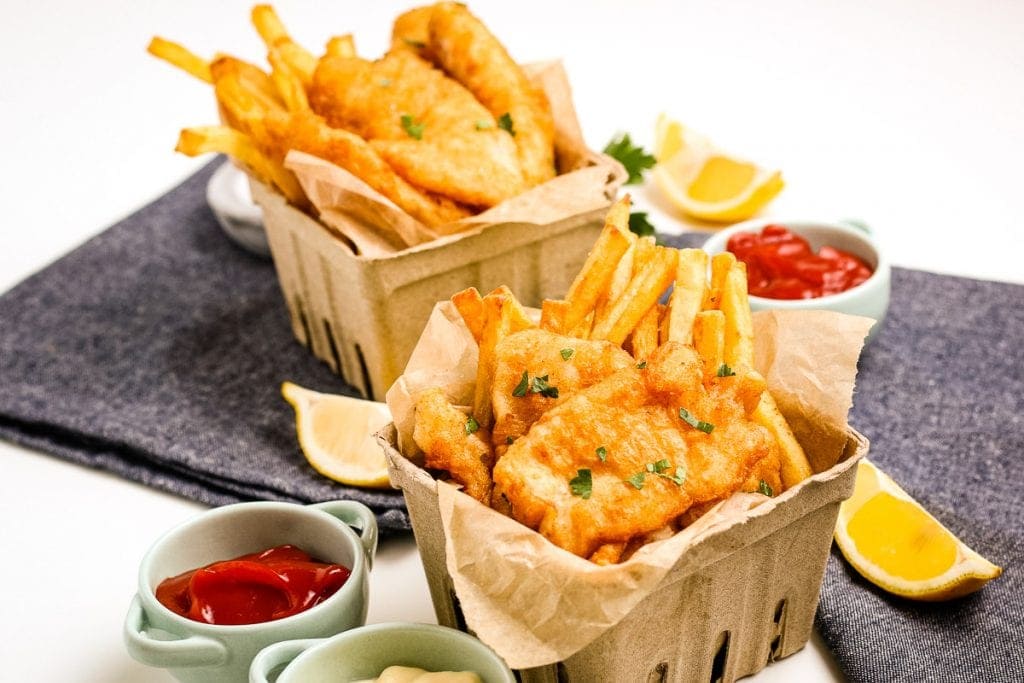 Beer Battered Fish and Chips  in cardboard containers with containers of ketchup and lemon slices beside them.