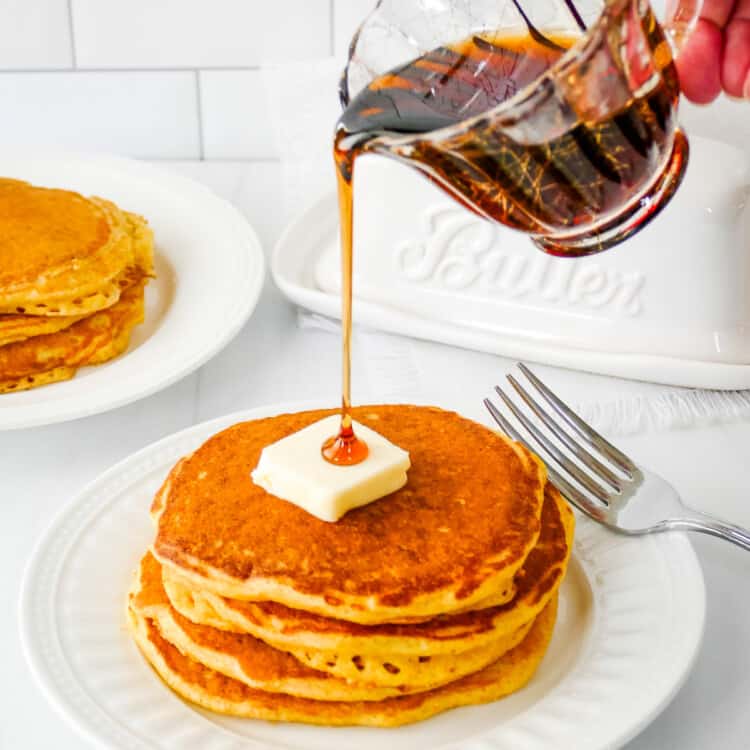 Small pitcher pouring syrup over the top of cornmeal pancakes