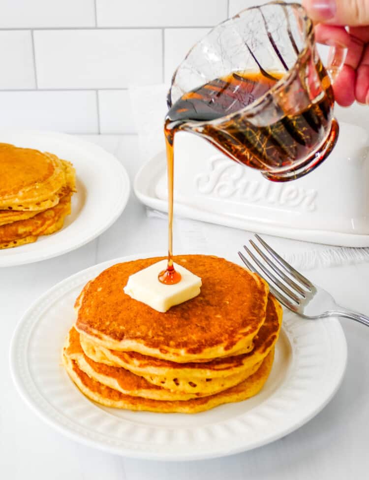Small pitcher pouring syrup over the top of cornmeal pancakes