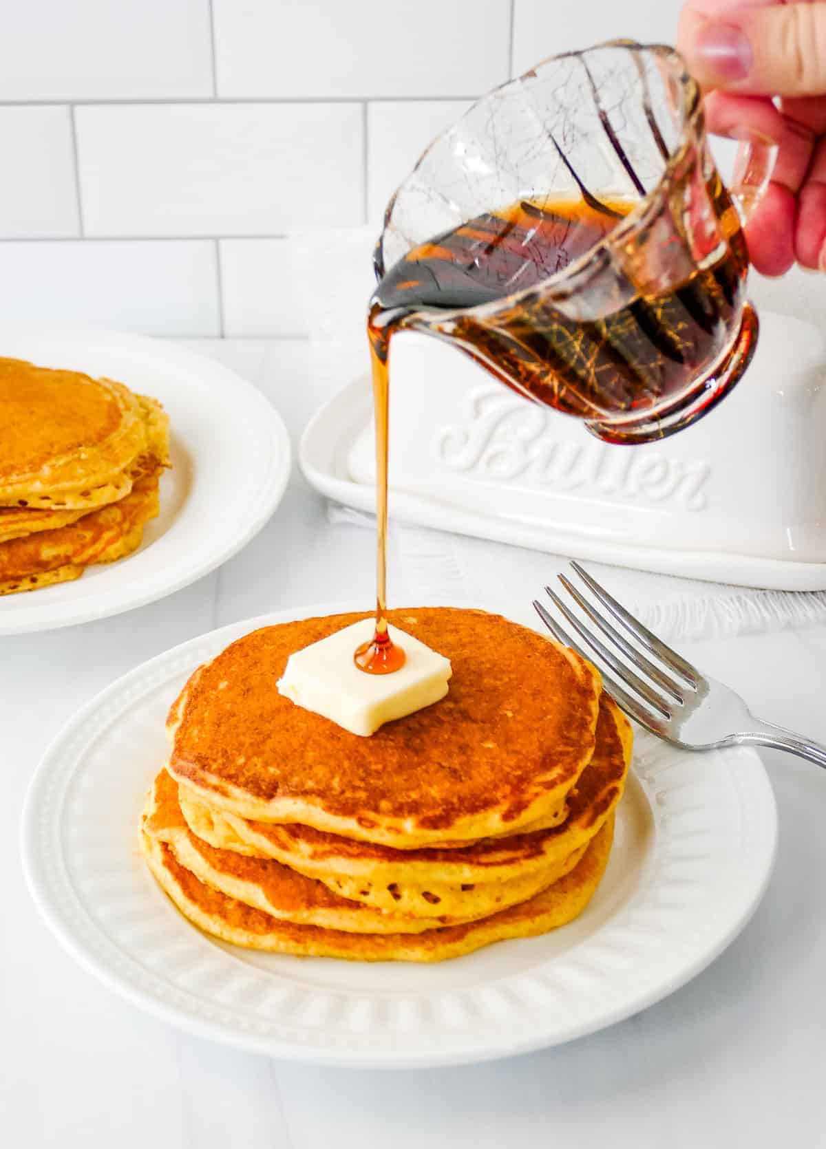 Small pitcher pouring syrup over the top of cornmeal pancakes