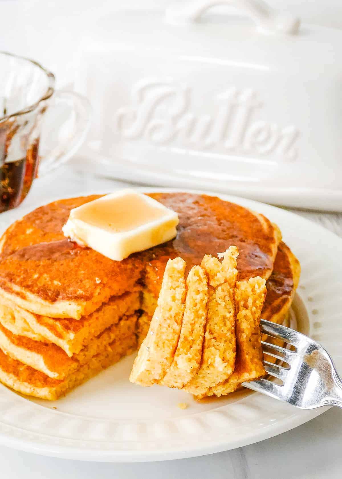 Plate with a stack of johnny cakes on it and a fork with a bite on it.