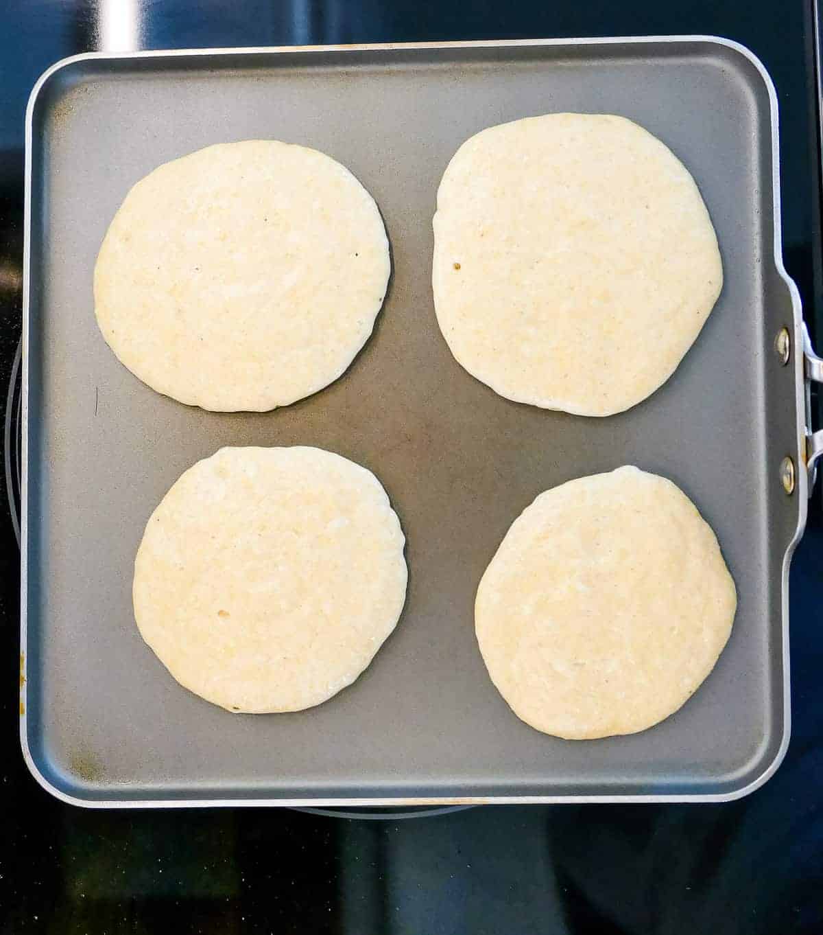 A square griddle pan with johnny cakes cooking on it