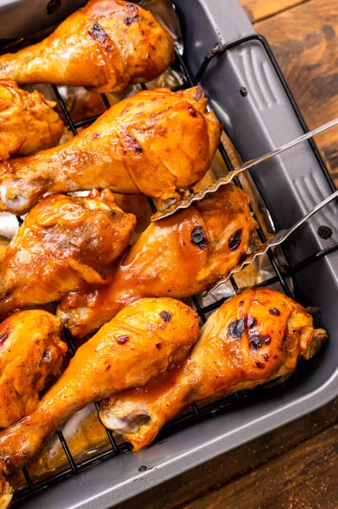 Tongs flipping chicken legs on wire rack on sheet pan